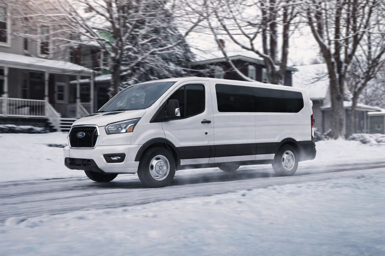 White Ford Transit van driving through a snowy residential street